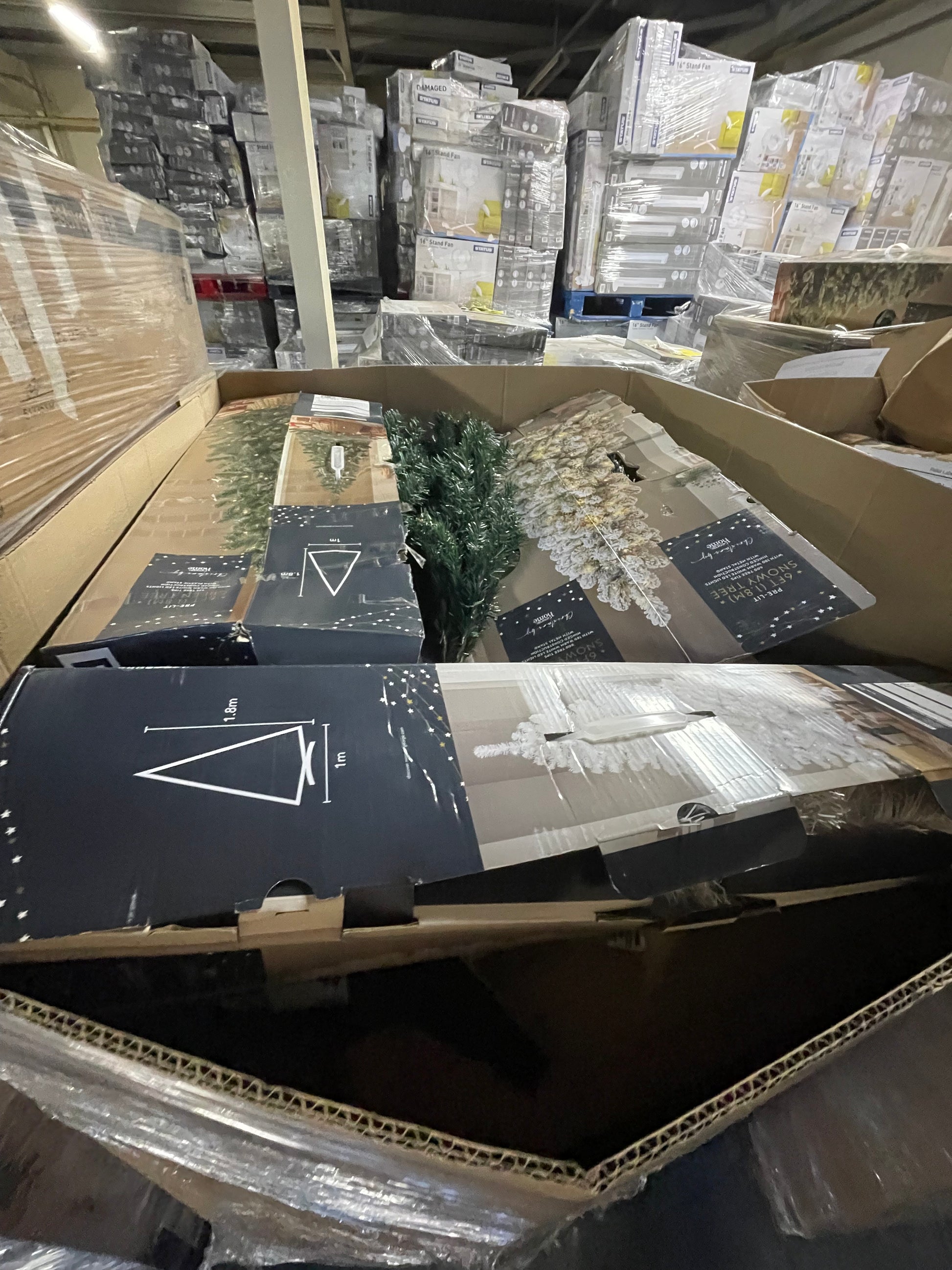 Wholesale Christmas tree pallets containing assorted holiday decorations and tree components stacked in a warehouse